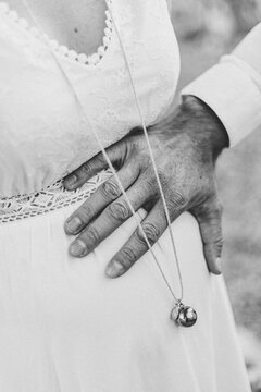 Un homme pose sa main sur le ventre d'une femme enceinte, habill&eacute;e d'une robe avec un collier