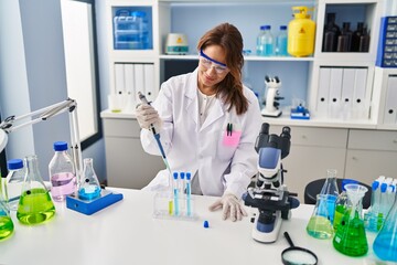 Fototapeta premium Young latin woman wearing scientist uniform using pipette working at laboratory