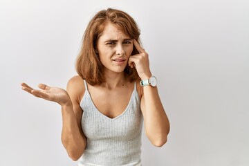 Beautiful caucasian woman standing over isolated background confused and annoyed with open palm showing copy space and pointing finger to forehead. think about it.