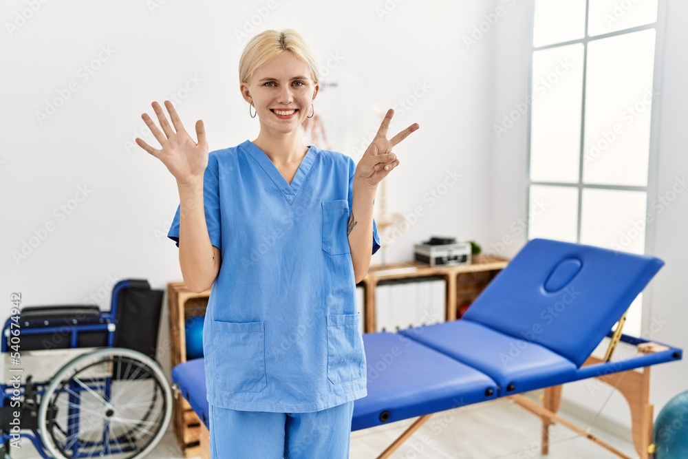 Sticker Beautiful caucasian physiotherapist woman working at pain recovery clinic showing and pointing up with fingers number seven while smiling confident and happy.