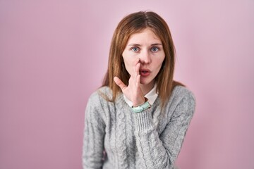 Fototapeta premium Beautiful woman standing over pink background hand on mouth telling secret rumor, whispering malicious talk conversation