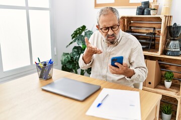 Senior grey-haired man using smartphone working at office