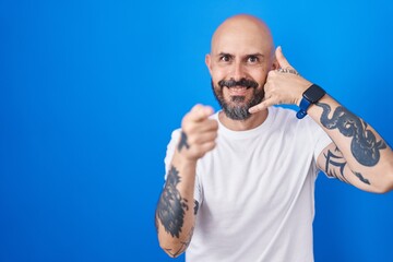Hispanic man with tattoos standing over blue background smiling doing talking on the telephone...