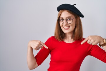 Young redhead woman standing wearing glasses and beret looking confident with smile on face,...