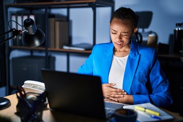 Beautiful african american woman working at the office at night with hand on stomach because indigestion, painful illness feeling unwell. ache concept.