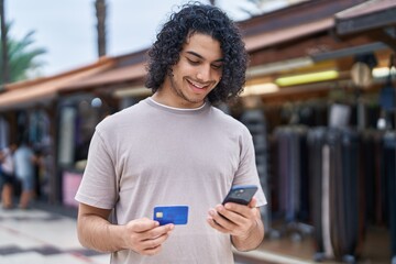 Young latin man using smartphone and credit card at street market