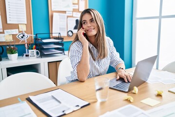 Obraz premium Young beautiful hispanic woman business worker using laptop talking on smartphone at office