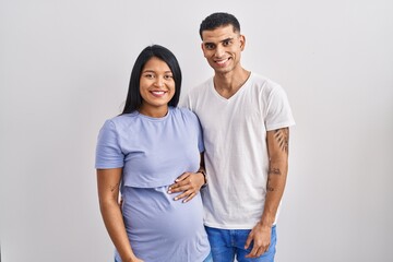 Young hispanic couple expecting a baby standing over background with a happy and cool smile on...