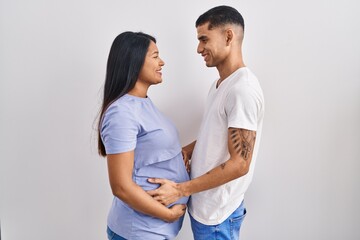 Fototapeta premium Young hispanic couple expecting a baby standing over background looking to side, relax profile pose with natural face and confident smile.