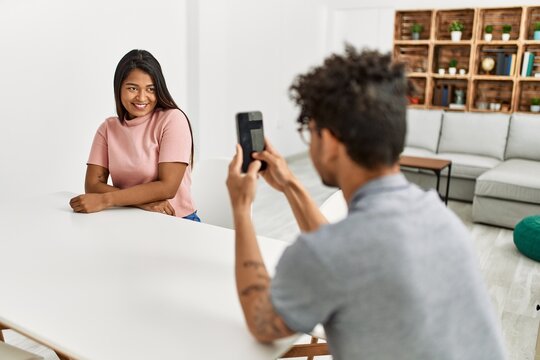 Young latin man making woman picture using smartphone at home.