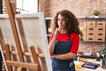 Young hispanic woman artist looking draw with doubt expression at art studio