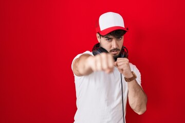 Hispanic man with beard wearing gamer hat and headphones punching fist to fight, aggressive and angry attack, threat and violence