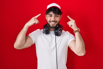 Hispanic man with beard wearing gamer hat and headphones smiling pointing to head with both hands finger, great idea or thought, good memory