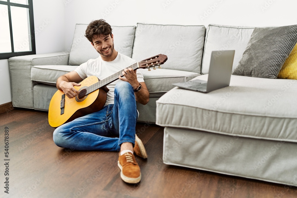 Wall mural young hispanic man smiling confident playing classical guitar at home