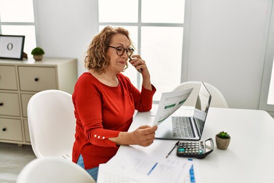 Middle age caucasian woman talking on the smartphone working at home.