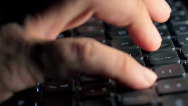 Close up footage of young businessman fingers busy working, searching and studying by typing on glowing keyboard in the dark for send emails and surf on a web browser,