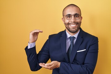 Hispanic man with beard wearing suit and tie gesturing with hands showing big and large size sign, measure symbol. smiling looking at the camera. measuring concept.