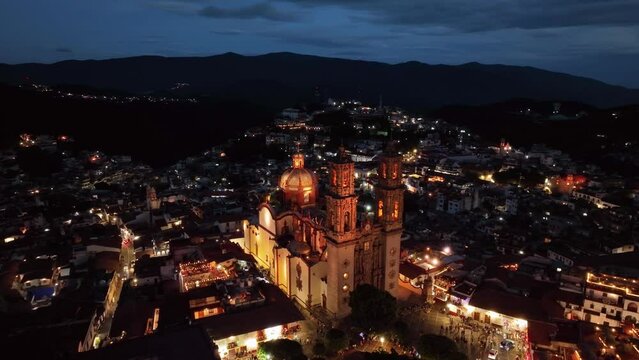 Aerial view around the night lit church of Santa Prisca, in Taxco Guerrero, Mexico - circling, drone shot