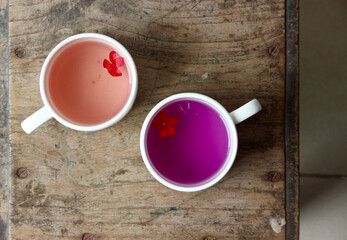 two white ceramic or porcelain cups filled with beautiful peach magenta colours flower tea with red flowers placed side by side on a wooden table as a offering to guests at home or at a cafeteria 