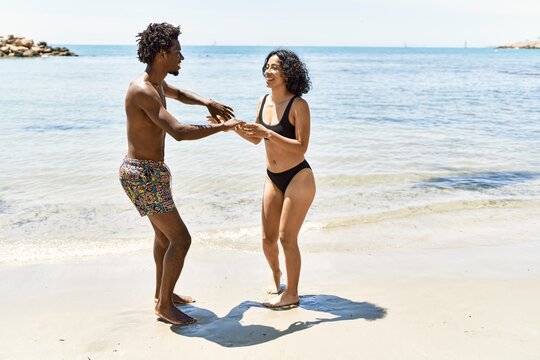 Young interracial tourist couple wearing swimwear dancing at the beach.