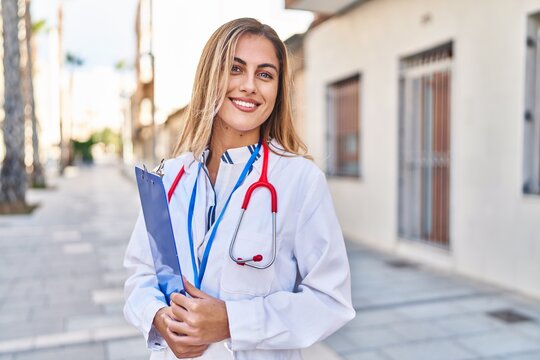 Young blonde woman wearing doctor uniform holding checklist at street
