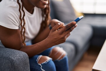 African american woman using smartphone sitting on sofa at home