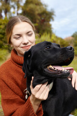 a happy woman hugs her black labrador dog while walking in an autumn park