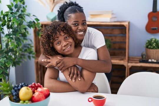African american women mother and daughter hugging each other drinking coffee at home