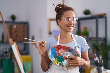 Young woman artist holding paintbrushes and palette at art studio