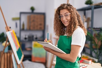 Young beautiful hispanic woman artist smiling confident drawing on notebook at art studio