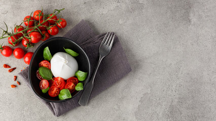 Burrata cheese with tomatoes and basil in a plate on a gray stone kitchen table, top view. Burrata cheese ball made from mozzarella and cream. Italian cuisine