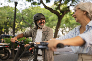 Obraz premium Smiling senior couple having fun riding an electric scooter