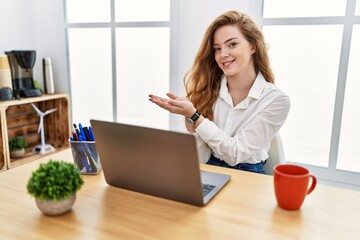 Young caucasian woman working at the office using computer laptop pointing aside with hands open palms showing copy space, presenting advertisement smiling excited happy