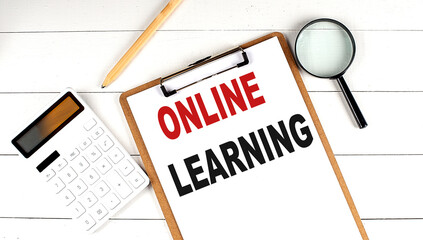 ONLINE LEARNING words on clipboard, with calculator, magnifier and pencil on the white wooden background