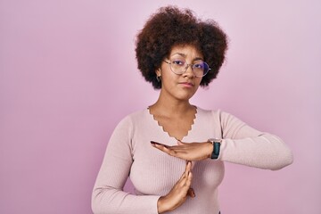 Young african american woman standing over pink background doing time out gesture with hands,...