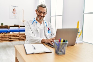 Middle age grey-haired man doctor using laptop working at rehab clinic