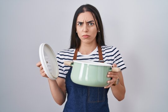 Young brunette woman wearing apron holding cooking pot skeptic and nervous, frowning upset because of problem. negative person.