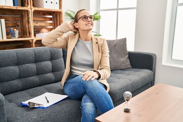 Obraz premium Young woman working at consultation office smiling confident touching hair with hand up gesture, posing attractive and fashionable