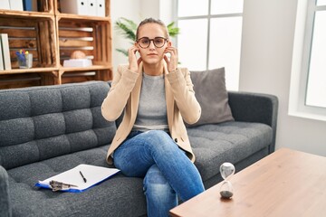 Obraz premium Young woman working at consultation office covering ears with fingers with annoyed expression for the noise of loud music. deaf concept.