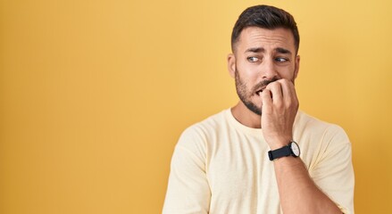 Handsome hispanic man standing over yellow background looking stressed and nervous with hands on...