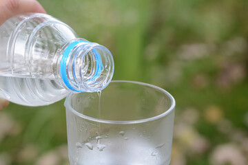 Woman pouring water from bottle into glass outdoors, closeup