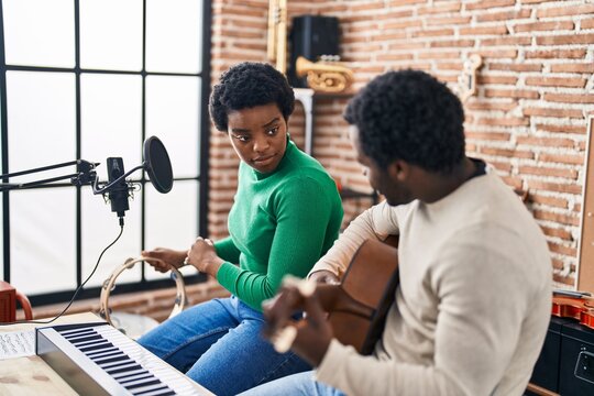 African american man and woman music group singing song playing guitar and tambourine at music studio