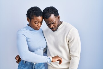 Obraz premium Young african american couple standing over blue background checking the time on wrist watch, relaxed and confident