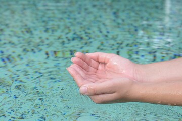 Girl holding water in hands above pool, closeup