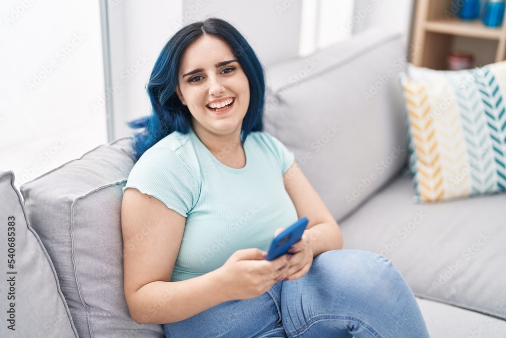 Poster Young caucasian woman using smartphone sitting on sofa at home