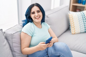 Young caucasian woman using smartphone sitting on sofa at home
