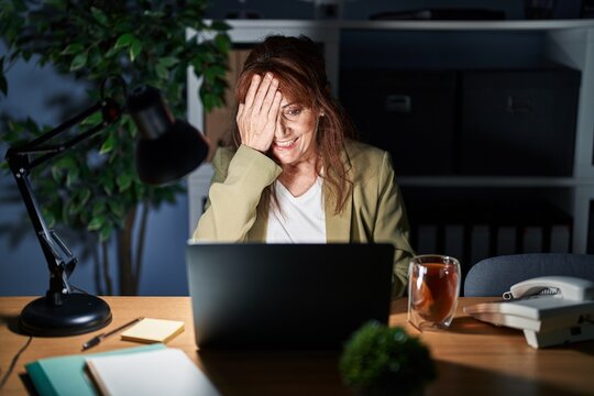 Middle Age Hispanic Woman Working Using Computer Laptop At Night Covering One Eye With Hand, Confident Smile On Face And Surprise Emotion.