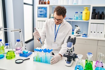 Young hispanic man scientist pouring liquid on test tubes at laboratory