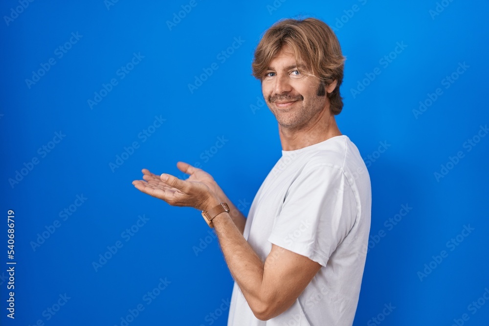 Poster Middle age man standing over blue background pointing aside with hands open palms showing copy space, presenting advertisement smiling excited happy