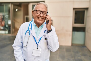 Senior man wearing doctor uniform talking on the smartphone at street